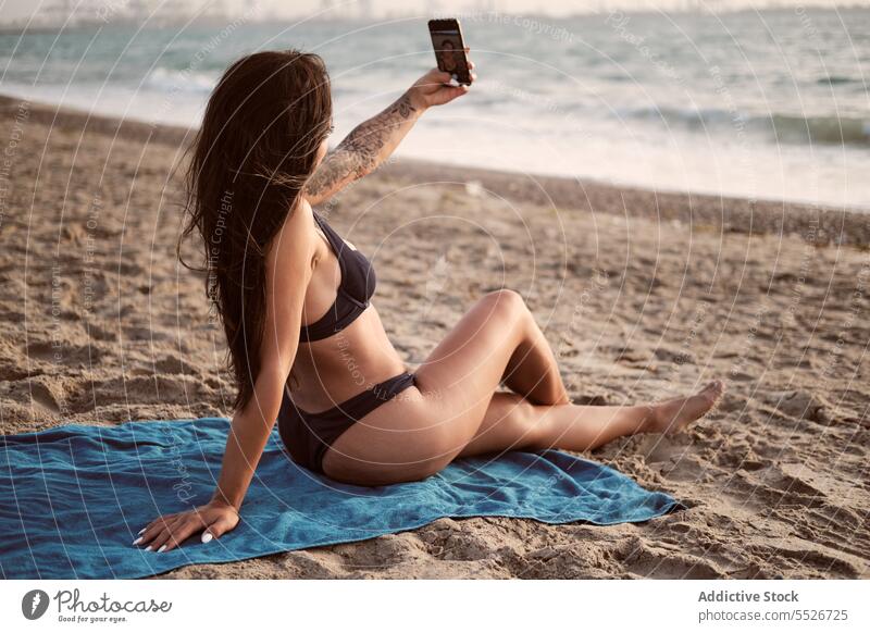 Slim woman in bikini taking selfie on beach smartphone using sand blanket summer vacation female rest device gadget relax swimwear summertime attractive