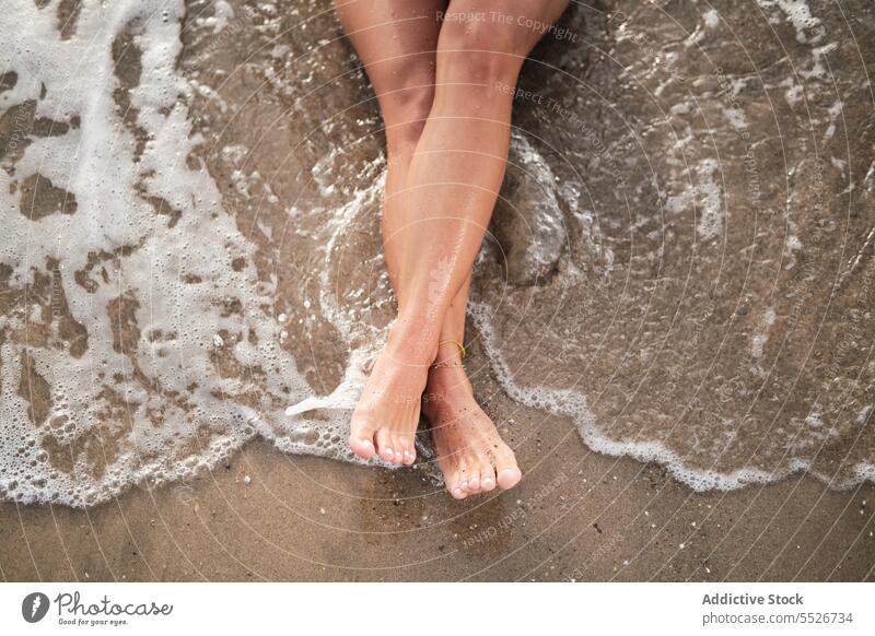 Crop legs of woman relaxing on wet sandy beach barefoot vacation summer foam water sea rest coast shore recreation seashore body part nature seaside carefree