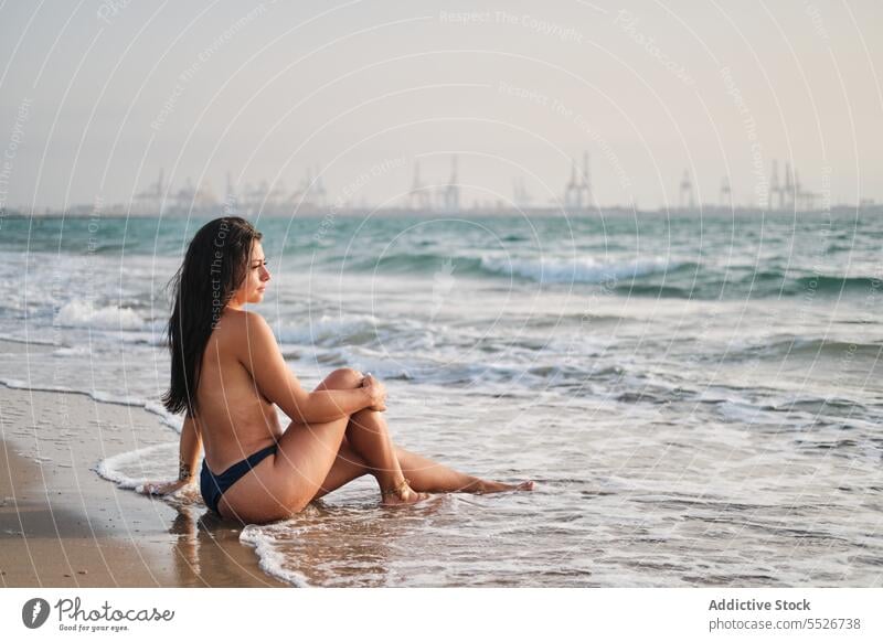 Topless woman relaxing in seawater on shore topless sensual beach seashore foam summer vacation wet hair sand coast female ocean rest slim naked recreation