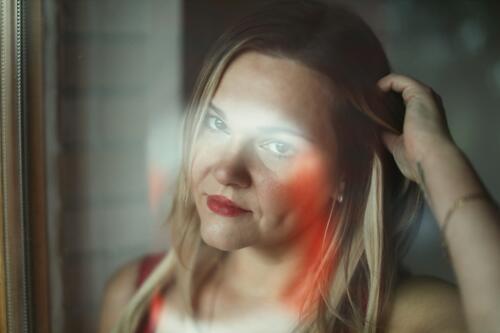 Blonde woman looks through a window pane with reflections directly into the camera - in the pane is the reflection of a life ring Woman portrait Long-haired