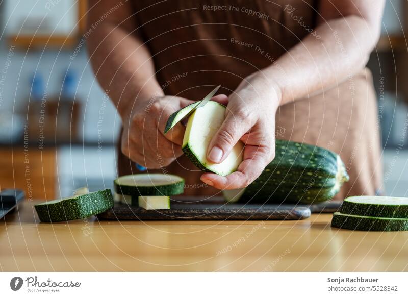 A woman peels a zucchini on a cutting board in a kitchen. Zucchini Woman Vegetable Cooking Food Lunch Vegetarian diet Organic produce Healthy Eating