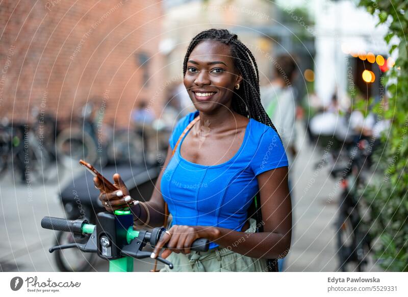 Portrait of happy young woman using her smartphone while standing with electric scooter in the city adult attractive beautiful black confidence confident cool