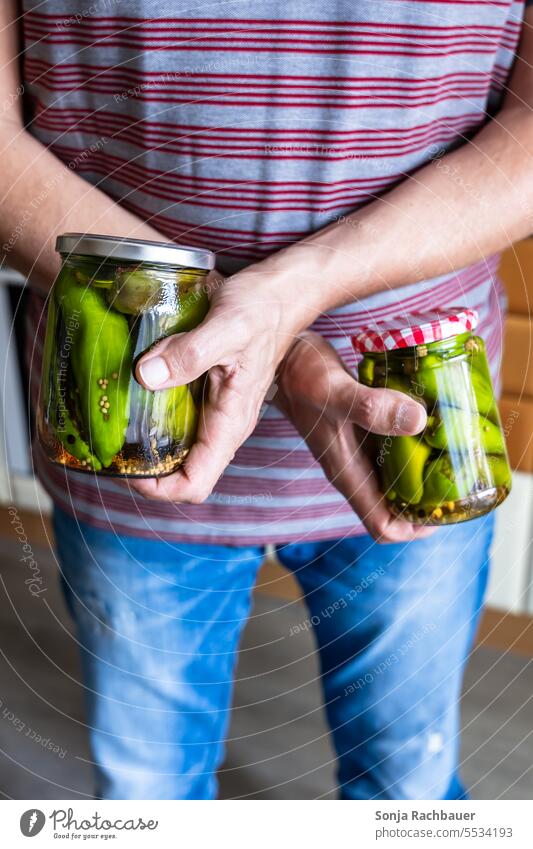 A man holds two jars with pickled peppers in his hands Preserving jar pepperoni Man stop Close-up 50 to 60 years Colour photo Pepper Conserve Self-made T-shirt