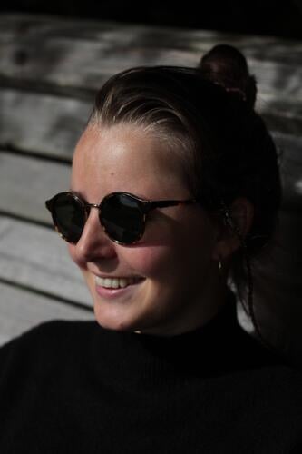 Beautiful woman with sunglasses Sunglasses Woman Laughter beautiful teeth Chignon Black youthful Wooden bench Sit Shadow play Sunlight sunshine Joy pleased