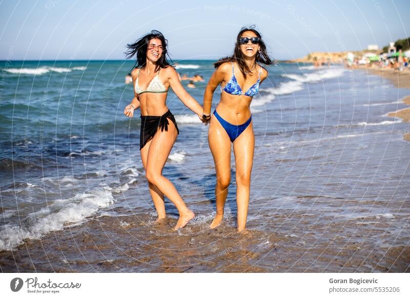 Two pretty young woman having fun on the seaside adult beach beautiful bikini carefree cheerful enjoy enjoyment female free time friends friendship happiness