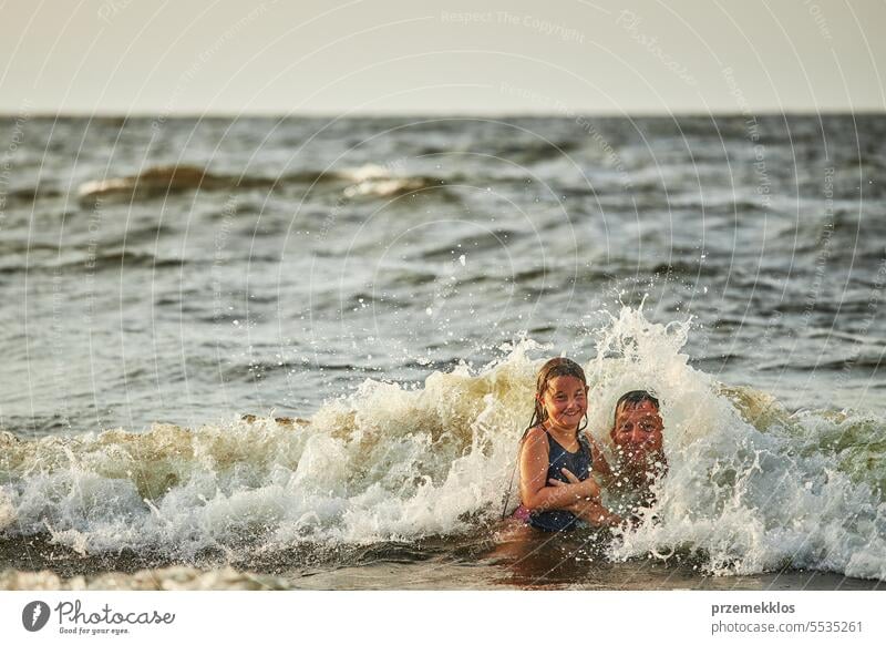 Little girl and her dad playing with waves in the sea. Family summer vacations. Kid playfully splashing with waves. Summer vacation on the beach ocean family