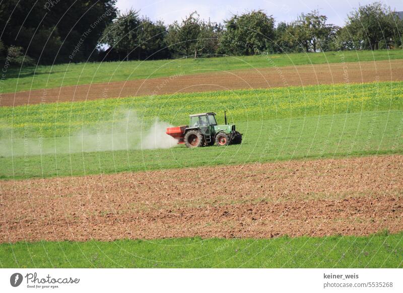 A tractor drives across the field with dusty fertilizer and the farmer does classic farming Agriculture peasant Tractor acre Dust Field glyphosate Farmer