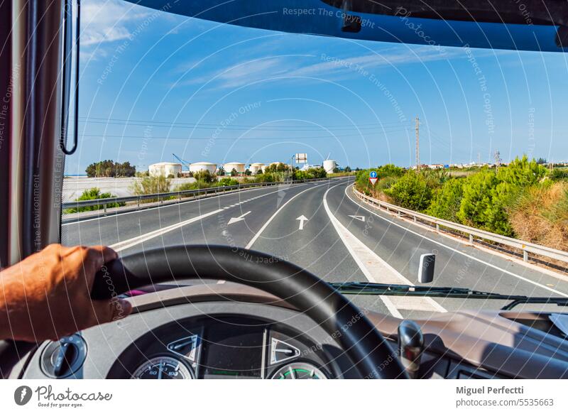 View from the driving position of a truck of a road leading to fuel tanks. inside steering wheel dashboard cab traffic storage tanks logistic transport hand