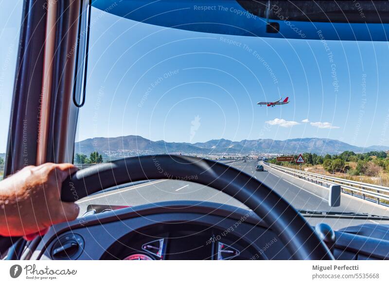 View from the driving position of a truck on a highway where a passenger plane prepared to land crosses, flying at low altitude. inside steering wheel dashboard