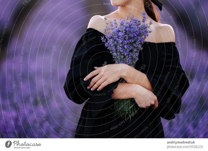 Young romantic woman with healthy natural beauty skin holding bouquet in lavender field. Beautiful girl wearing black dress and bow on hair. Advertising natural product