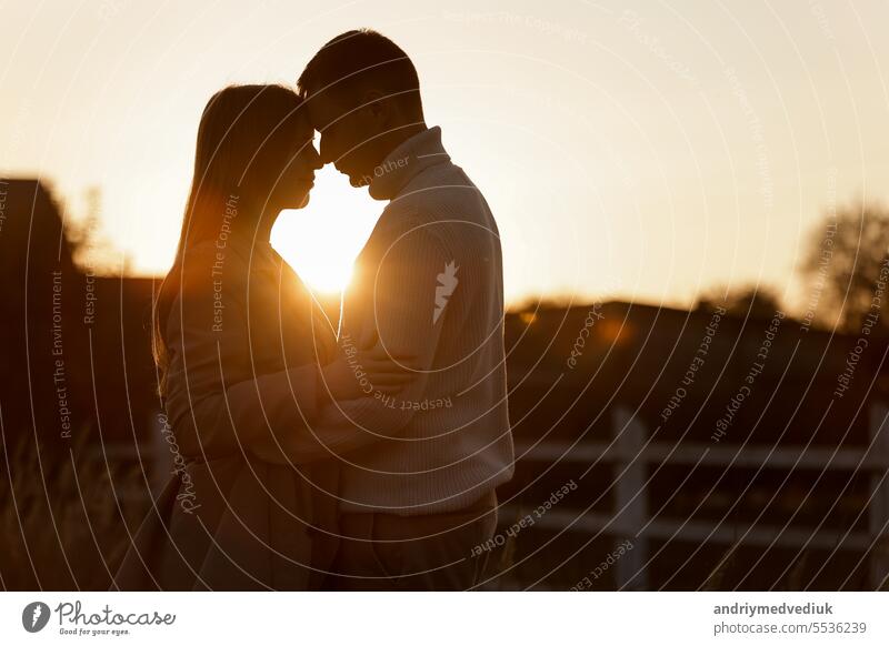 Silhouette of loving couple couple at sunset is hugging and touching nose to nose outdoors at park. Young man and woman falling in love have romantic date on Valentine's day