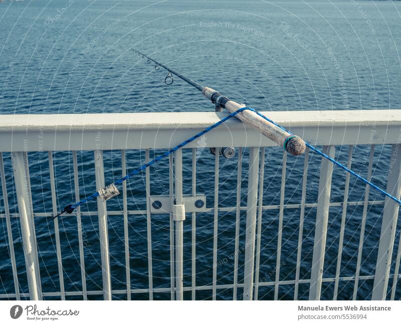 A fishing rod is attached to a bridge handrail over a lake. - a