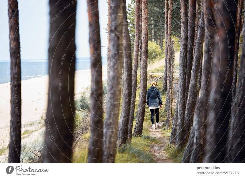 Woman hiking in forest along seashore. Person actively spending vacations. Summer trip. Enjoying walking at sea coast. Outdoor activity summer beach destination