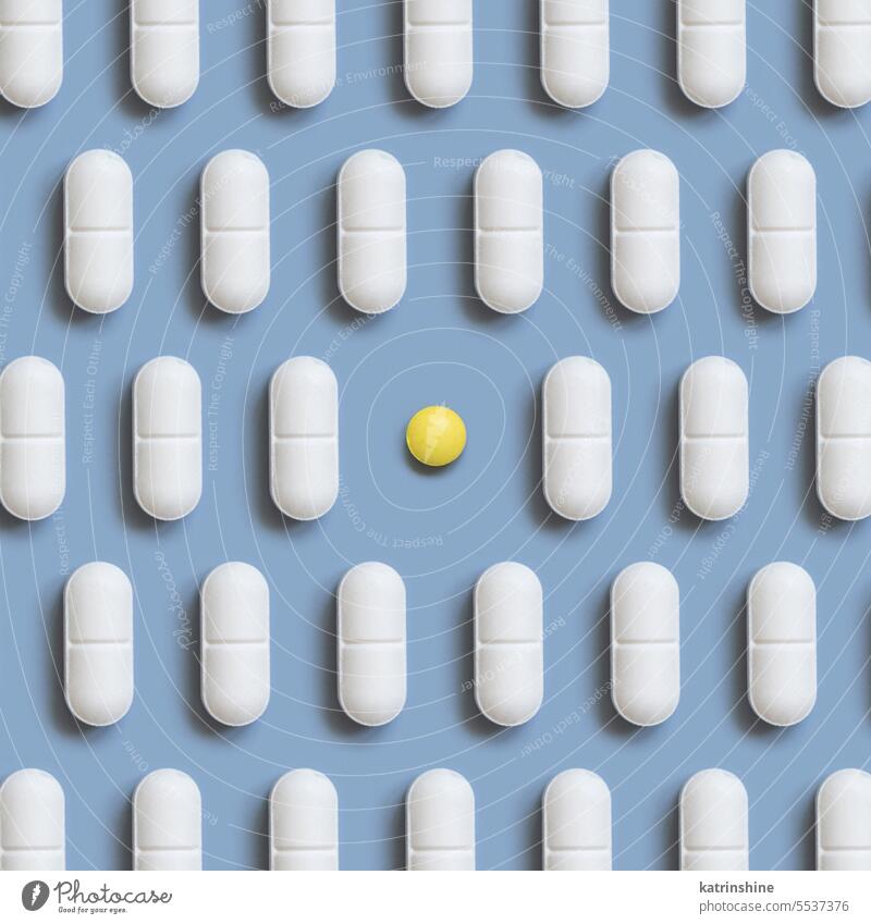 Mix of white medical pills in a line with one yellow on light blue top view. Dietary supplements medicine pharmaceutical capsules vitamins difference creative