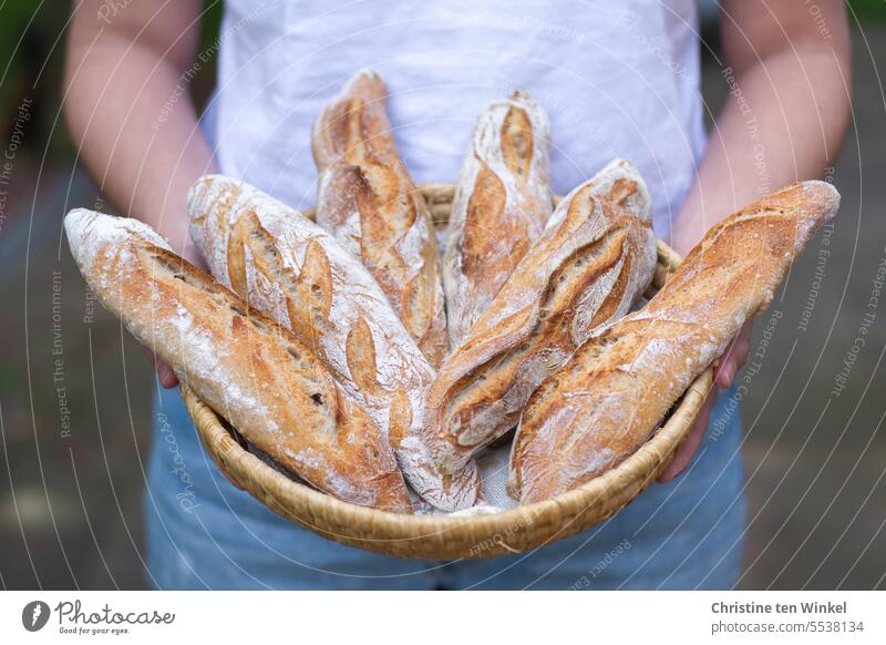 The young woman proudly presents the homemade baguettes Baguettes Rustic Young woman Bread basket Tradition Crust Crisp tastily luscious Aromatic Fresh Tasty