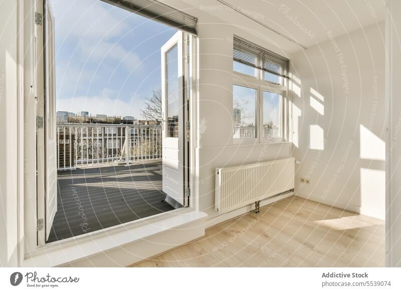 White room with window and door leading towards balcony white modern apartment sunny interior radiator sunlight floor railing shadow wall copy space house