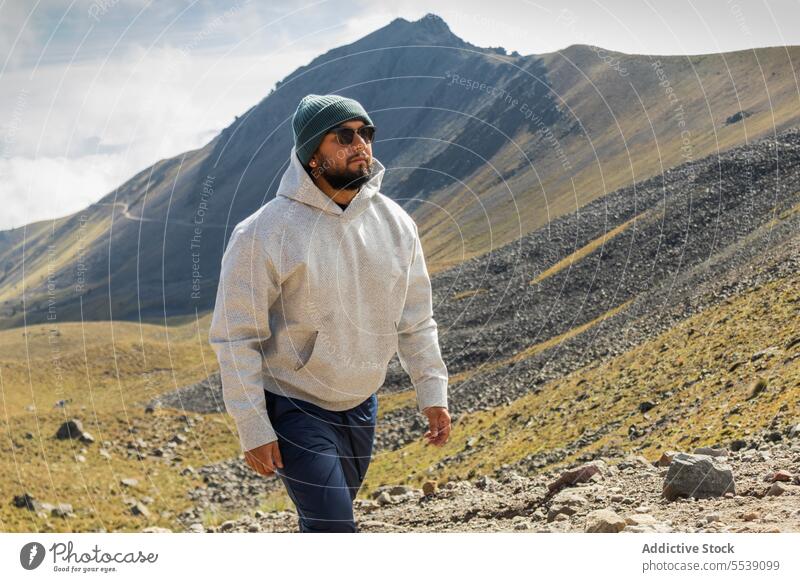 Young man walking on mountain cliff rock in daylight hiker landscape adventure tourist admire volcano nature male young path beard warm clothes lake smile