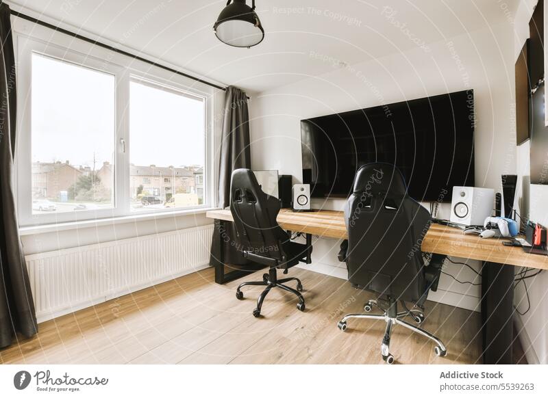 Home office with furniture and computer home office television desk empty chair large window bright apartment curtain black tv screen copy space technology