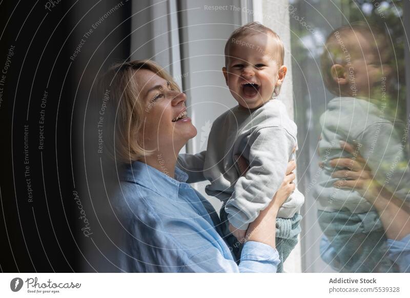 Mature blond woman and a baby boy near the window at home mother infant child love care childcare parent motherhood childhood family room parenthood bonding
