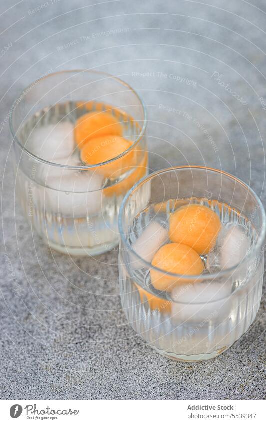 Glass with melon spheres in iced beverage placed on surface pair glass drink transparent serve cocktail daylight fresh bright refreshment cold ingredient tasty