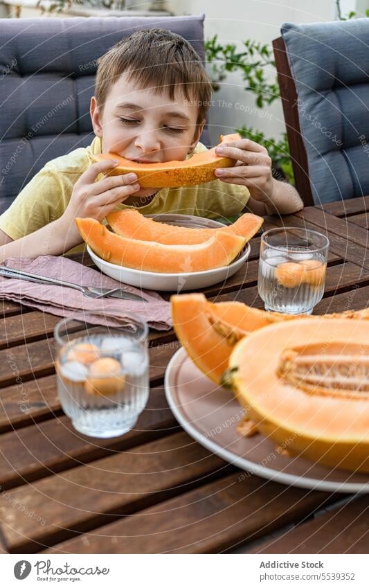 Preteen boy sitting at table and eating fresh cut musk melon preteen fruit healthy slice nature summer child refreshment drink beverage food kid breakfast