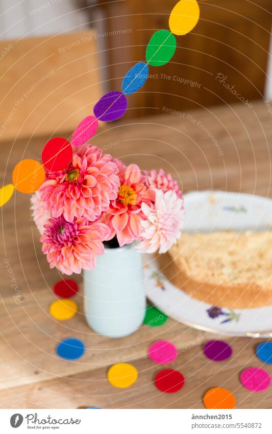 a bouquet of dahlias stands on a wooden table next to it is a cake and you can see a colorful garland and colorful confetti Birthday celebrations variegated