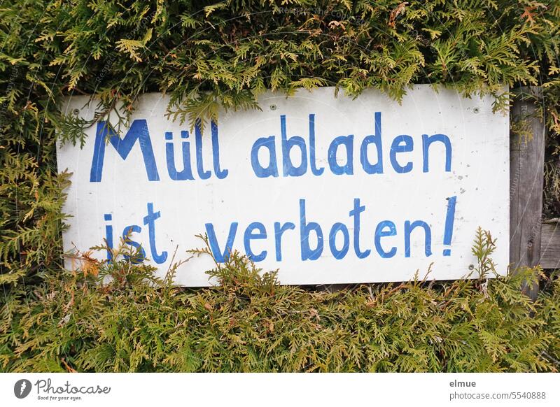 handwritten sign: dumping garbage is forbidden ! on the fence in a hedge Dumping garbage is prohibited Waste management no garbage dump rubbish dump