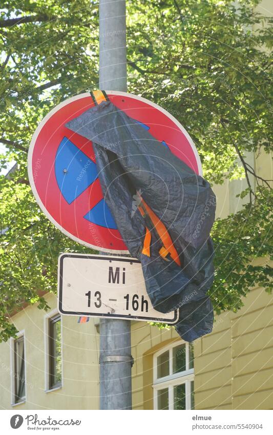 Traffic sign " Absolute no stopping " with additional sign for time restriction only partially covered with a plastic tarpaulin in front of a residential building