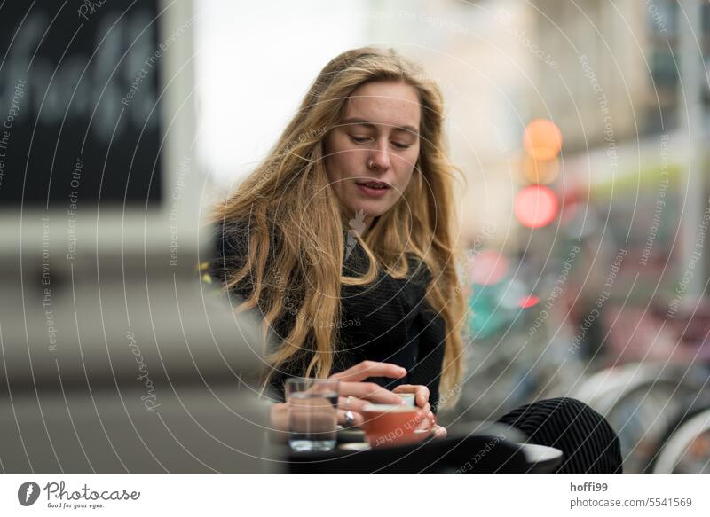 a young woman in a sidewalk coffee shop looks thoughtfully friendly at the coffee cup in her hand Face of a woman Young woman Adults Woman portrait