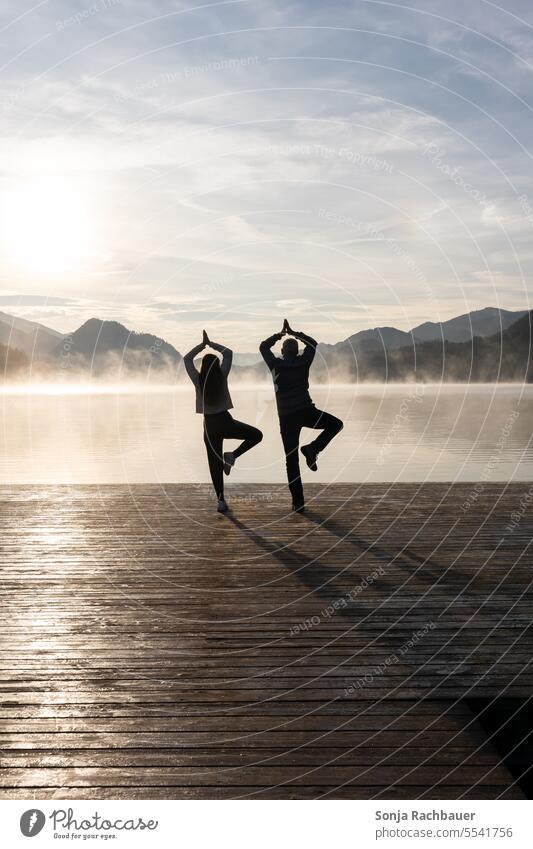 Father and daughter doing yoga on a wooden jetty by a lake. Morning sun, autumn. Man Woman Rear view Yoga Lake morning sun Sunrise Calm Idyll wooden walkway Fog