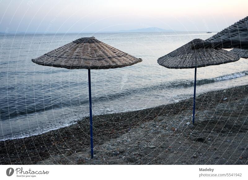 View from the beach in Altinoluk of wicker parasols in the romantic light of the setting sun and the Gulf of Edremit on the Aegean Sea in Balikesir province, Turkey