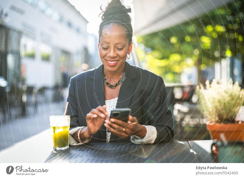 Portrait of a smiling businesswoman using mobile phone in outdoor cafe people downtown joy urban black natural attractive city black woman happiness street