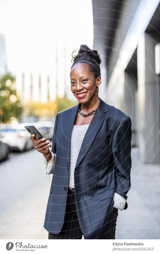 Portrait of smiling mature businesswoman using mobile phone in urban setting people downtown joy black natural attractive city black woman happiness street