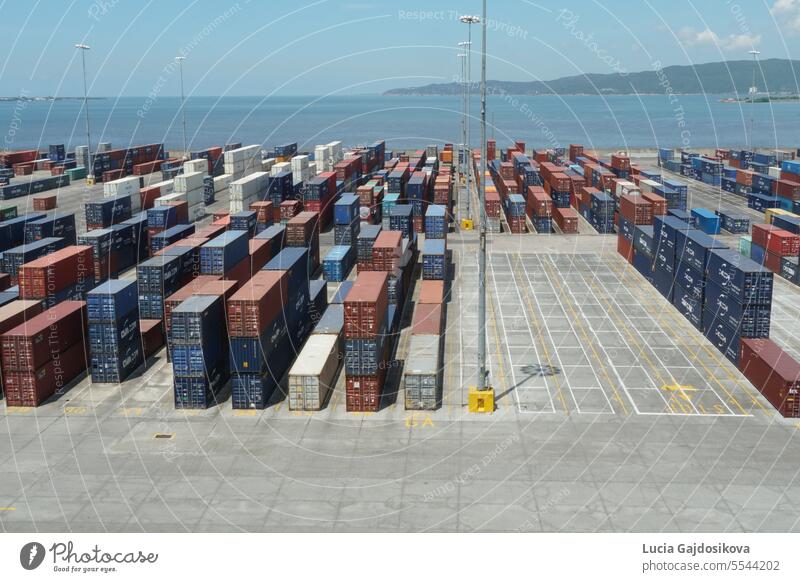 Container terminal with boxes from different shippers lined in the Port of Kingston, the most famous seaport of Jamaica. Behind are hills and Atlantic ocean.