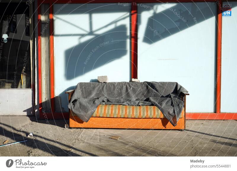 Old discarded striped sofa in green and orange with gray blanket in front of closed store in summer sunshine in Adapazari, Sakarya province, Turkey Sofa couch