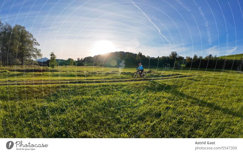 Weitwinkelaufnahme von einer Frau die im Gegenlicht der Sonne radfährt frau sport radfahren fahrrad abend sonne gegenlicht sonnenlicht fahrradfahrerin radlerin