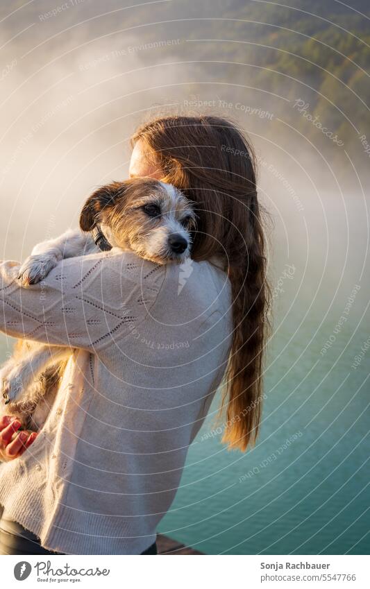 A small dog lies on the shoulder of a young woman by a lake Dog Pet Woman Friendship Love Together Animal Happy Lifestyle Cute Shoulder Embrace long hairs