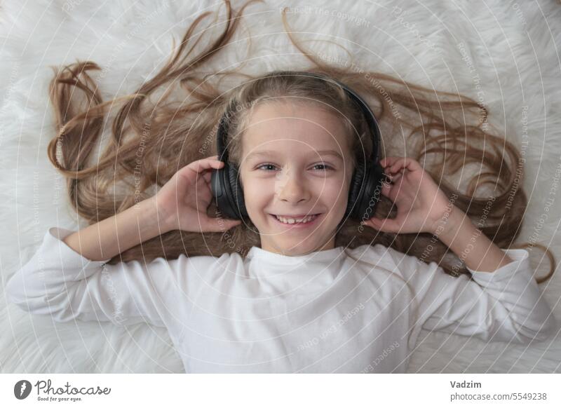 Little girl in wireless headphones on a white fur carpet close-up 5-10 years old Lifestyle Girl Introduction of modern technology Color image Copy space
