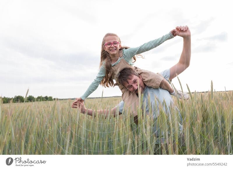 A girl and her father are happy and playing against the backdrop of an agricultural field. Light Walking Joy Day wax Ear ears Bread Rye Wheat Harvest Cereals