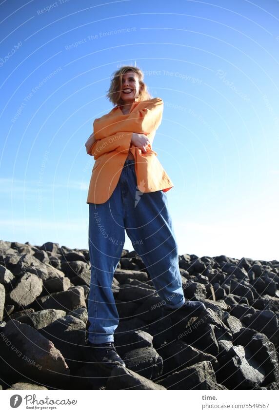 laughing woman on bean stones Woman Jacket Stand cross arms hair hairstyle Shadow breakwater Protection sunny Sky Laughter beanstones coast Beautiful weather