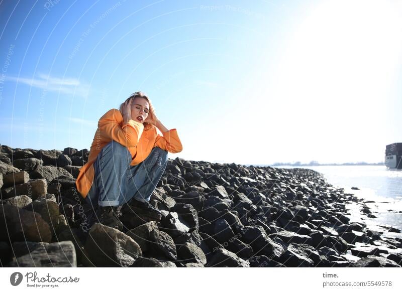 Woman, sitting on bean stones Jacket hair hairstyle Shadow breakwater Protection sunny Sky Beautiful weather coast beanstones Feminine Long-haired Blonde Gravel