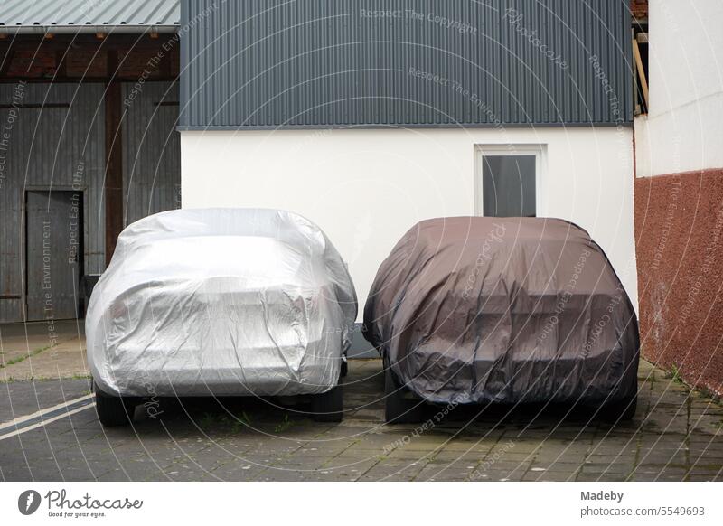 Two cars with car tarpaulin or tarpaulin in silver or light gray and brown in the courtyard of an old farm in Wettenberg Krofdorf-Gleiberg near Giessen in Hesse