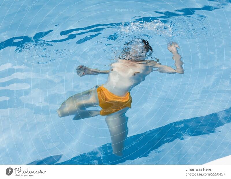 An inviting azure pool sets the stage for a playful scene. A topless girl is being underwater. Her sexy curves and orange bikini are in focus. Swimming drowning