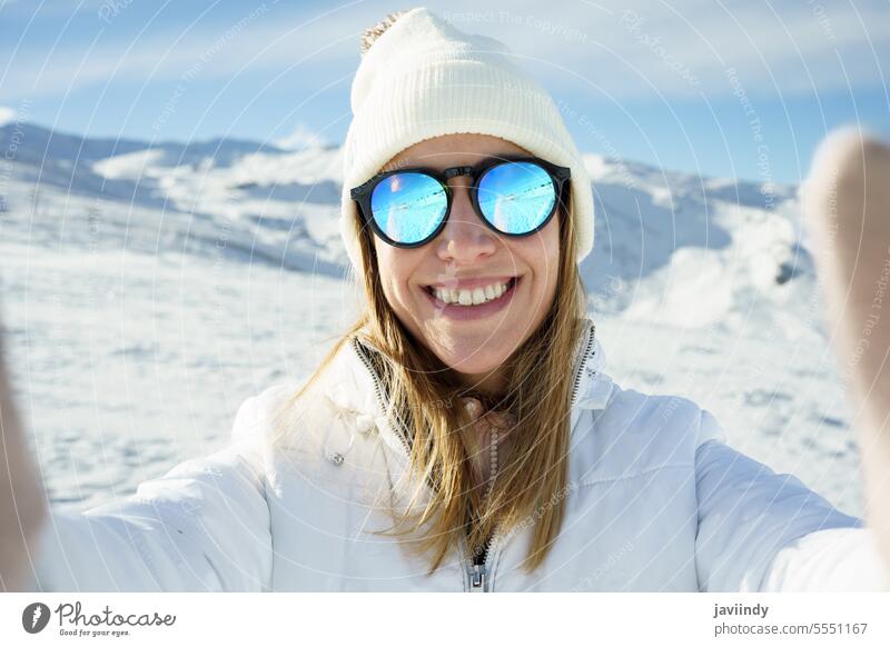 Cheerful woman in sunglasses taking selfie in snowy mountains winter smile happy warm clothes slope take photo female young optimist enjoy content season