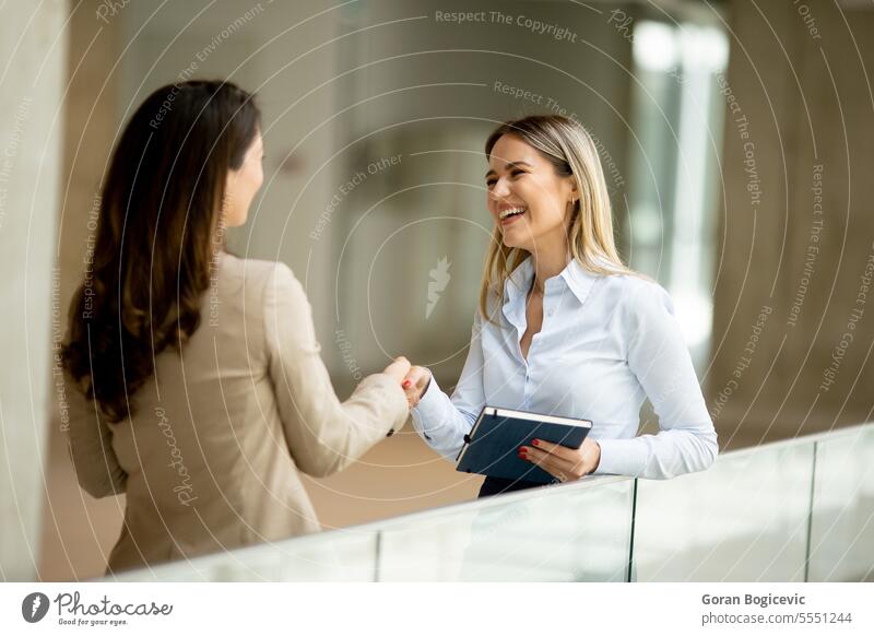 Two young business women with paper notebook in the office hallway adult businessman businesspeople businesswoman businesswomen caucasian ethnicity
