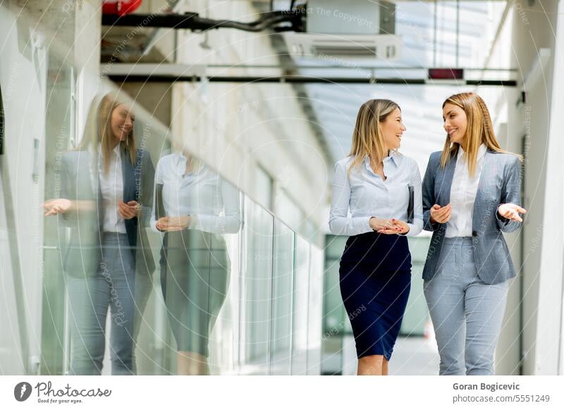 Two young business women walking and discussing in the office hallway adult businessman businesspeople businesswoman businesswomen caucasian ethnicity