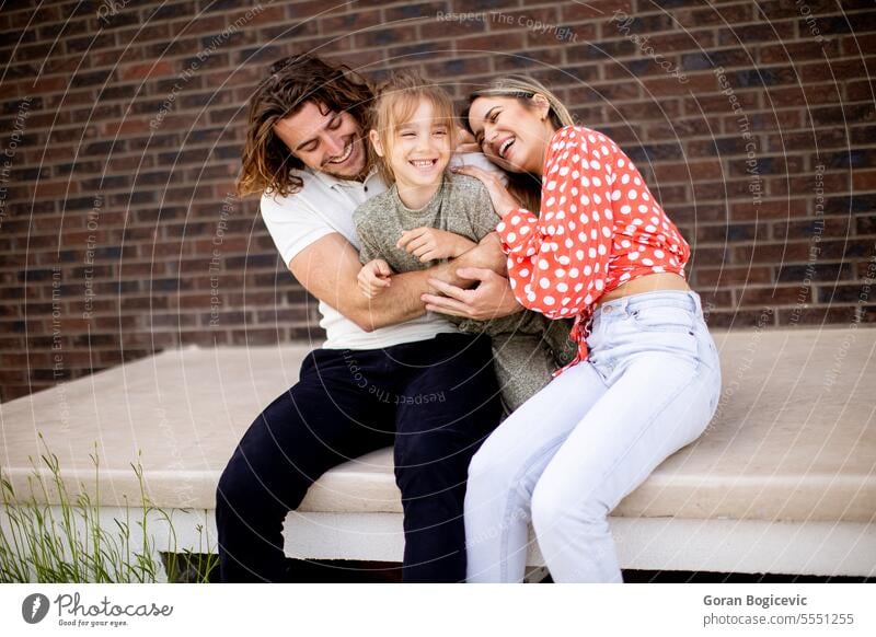 Family with a mother, father and daughter sitting outside on the steps of a front porch of a brick house adult adult man bonding child childhood couple dad