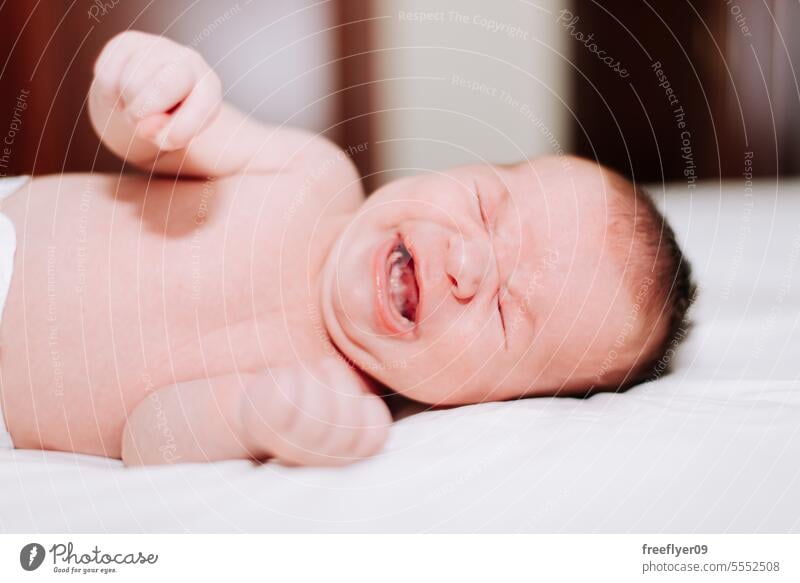 newborn crying in studio lighting against white baby firstborn portrait laying laying down copy space parenthood motherhood innocence life labor young boy happy