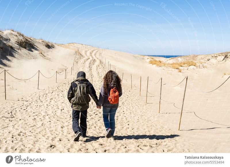 A man and a woman walk hand in hand on the sand dunes on the Curonian Spit near the Baltic Sea couple backpacker tourists travel shore male female two people