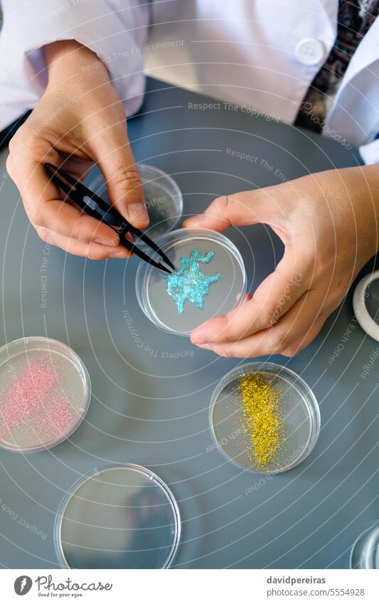 Unrecognizable female chemist technician examining a blue glitter sample over petri dish on lab unrecognizable hands analyzing micro plastic analysis laboratory